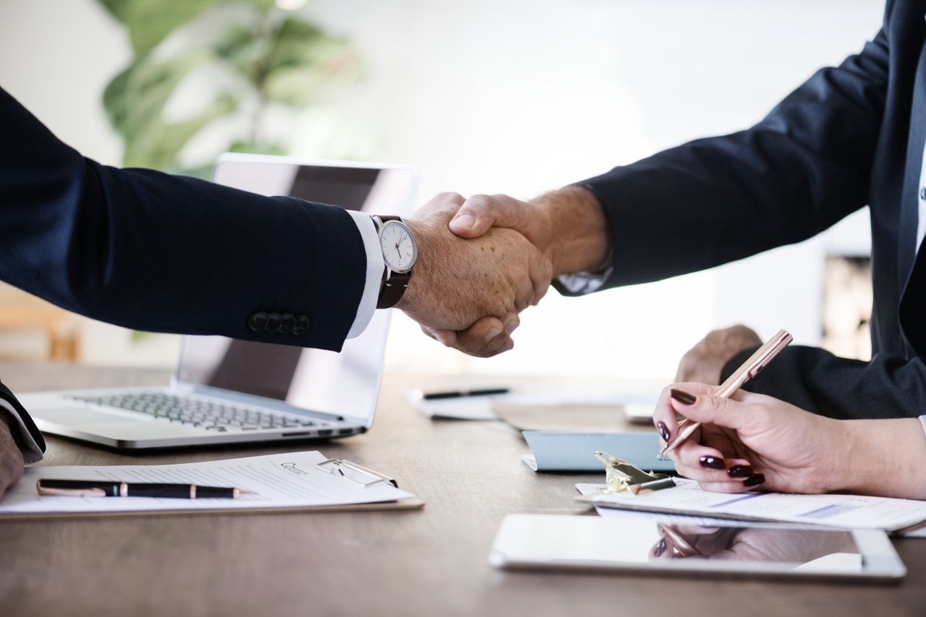 Two businessmen are shaking hands in office while sitting at the desk, close-up to represent Bad Credit Merchant Account