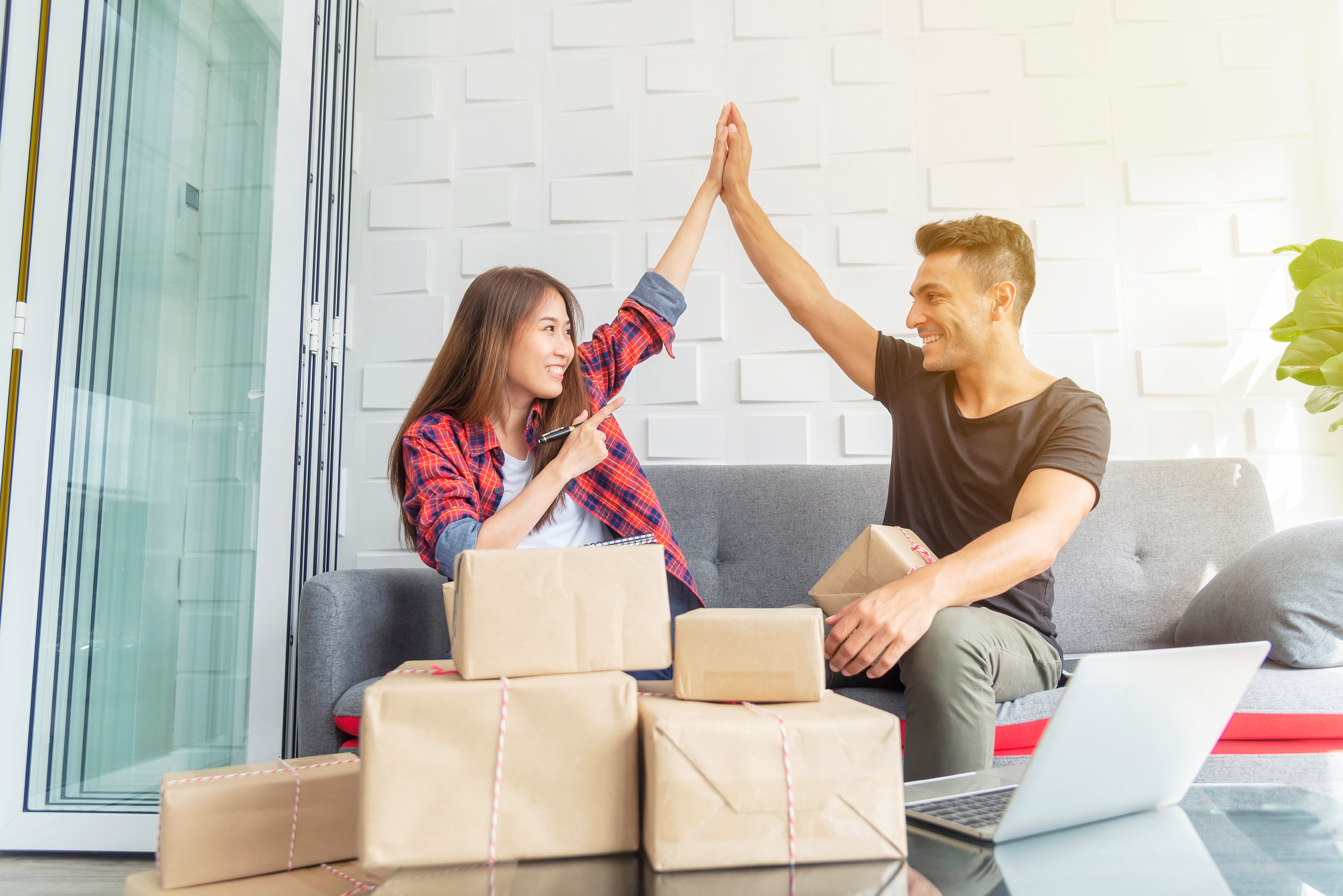 happy couple running online bussines high fiving success, with computer and shipping boxes around to show cbd oil purchase