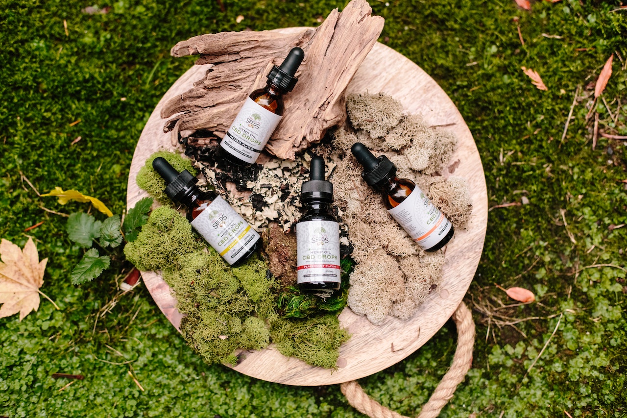 set of CBD products on log wooden display podium with nature leaves and grass around it 