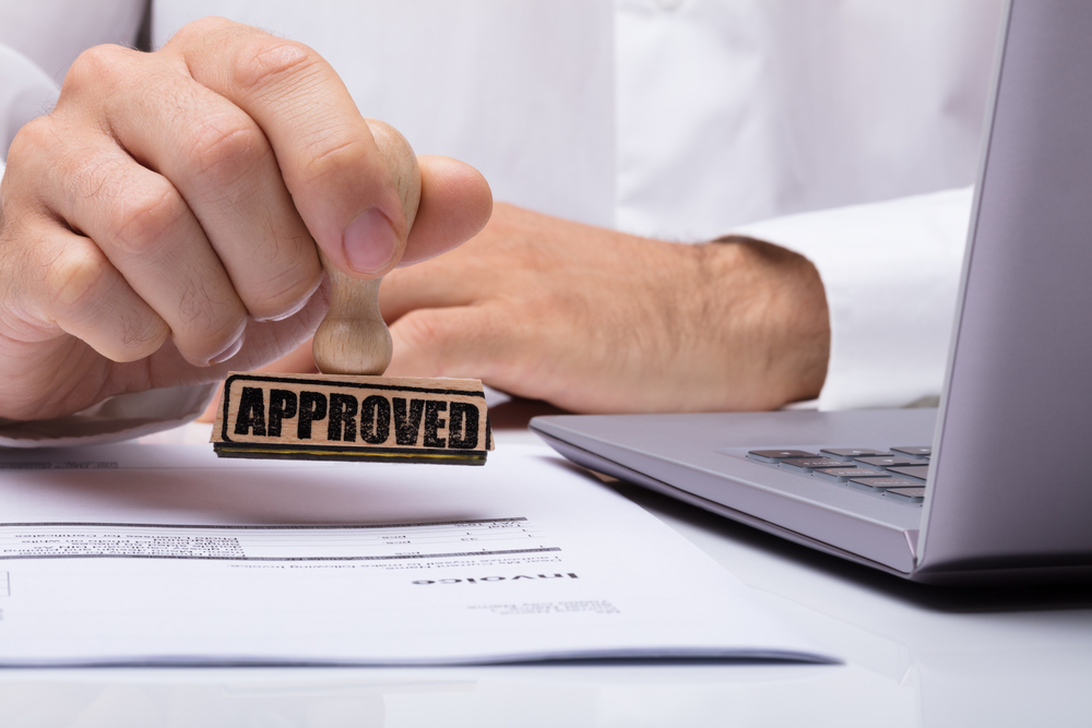 Close-up of a person's hand stamping with an approved stamp on a credit card merchant application at a desk