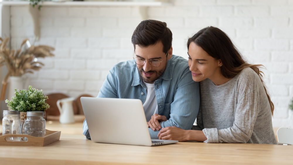 Happy young couple looking at laptop screen, checking finances, sitting at table at home together: Casino Merchant Account