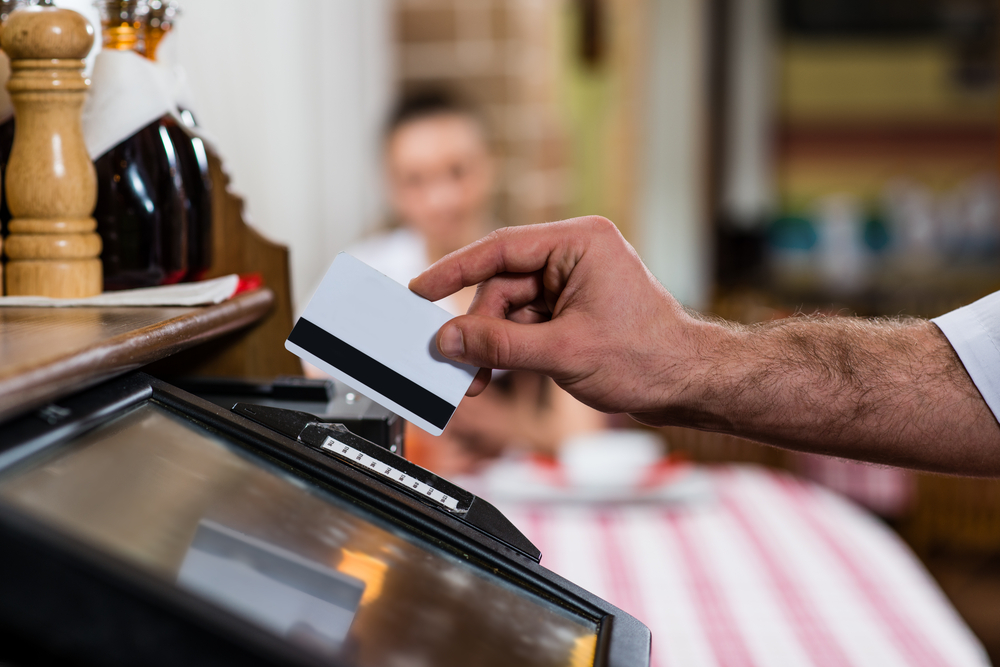 Close up of skillful male restaurant worker is swiping credit card through the screen to represent Online Merchant Account