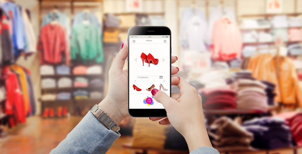 Woman in clothing store holding phone in hands and searching online shoes