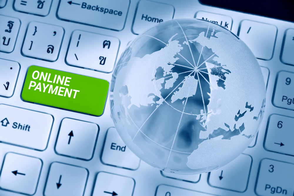 ONLINE PAYMENT inscribed on a green enter key button of a white desktop computer keyboard with a world globe map to represent easy merchant account