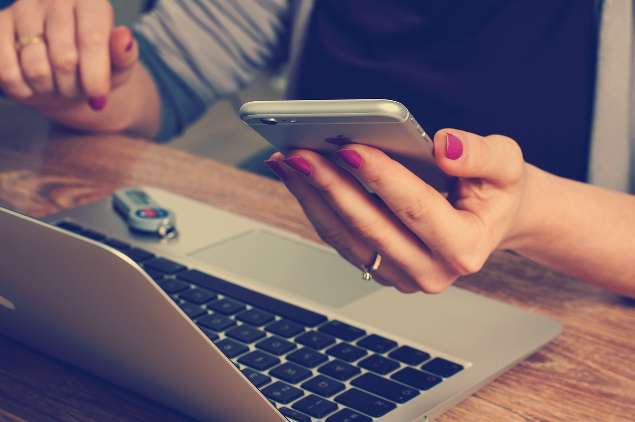 A person using their mobile phone and computer to log onto their merchant account.