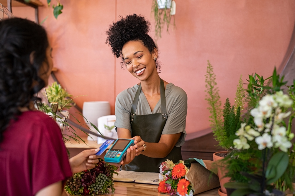 female customer stand near bar counter pay bill using credit card terminal to represent bigcommerce payment gateways