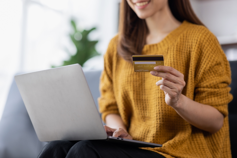 Bigcommerce Payment Gateways. smiling woman using laptop, holding and showing plastic debit credit card. 