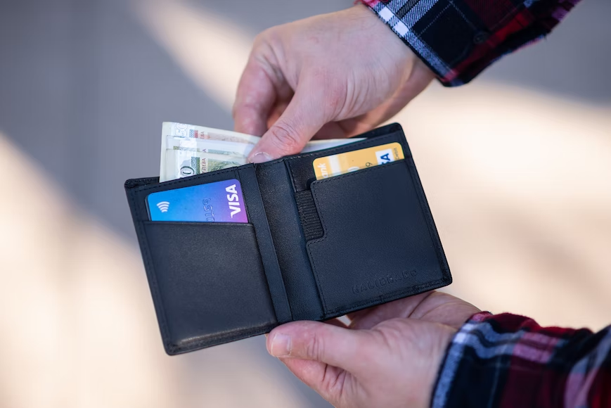 Man taking cash out of wallet with credit cards visible to symbolize different types of payment methods.