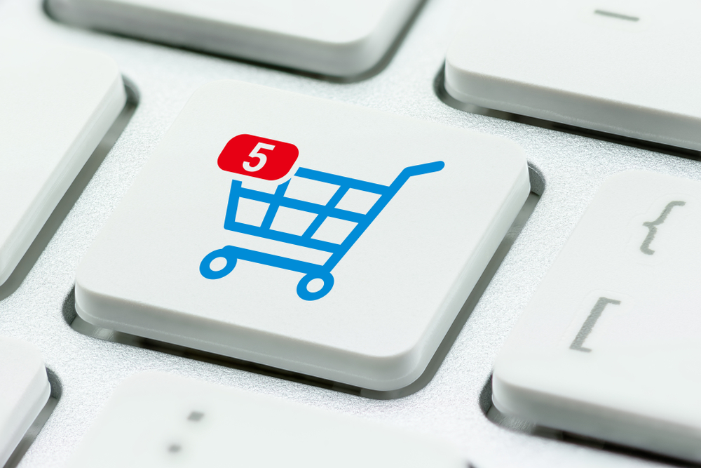 Online shopping / ecommerce and retail sale concept : Shopping cart with 5 items in a basket, a trolley symbol on a laptop keyboard, depicts customers order things from retailer sites using internet