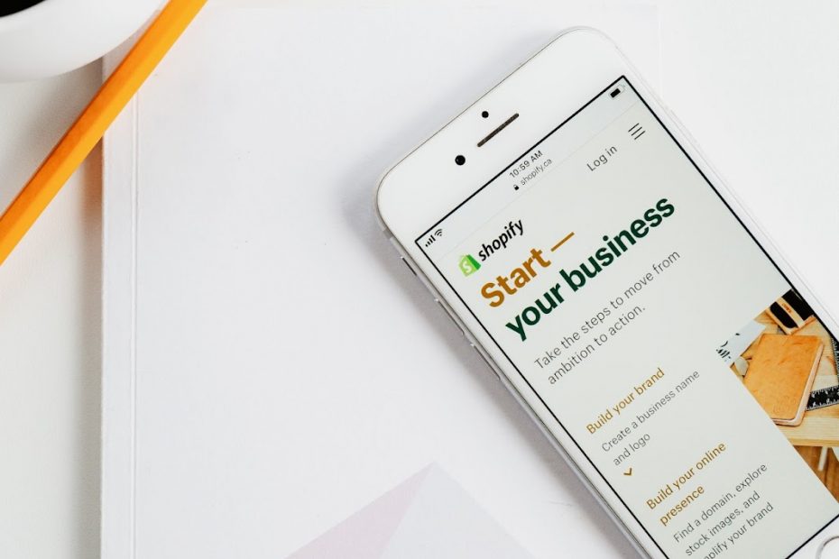 Phone sitting on top of a notebook with Shopify logo in bottom right corner, open to Shopify “Start Your Business” page