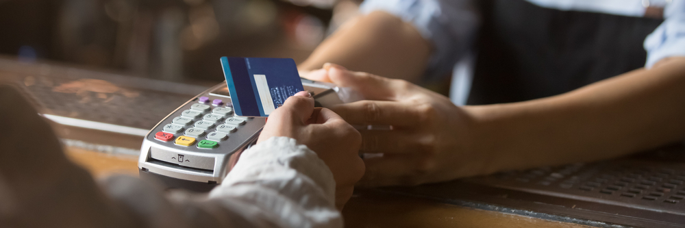 A customer paying a small business merchant on a POS terminal with a credit card.