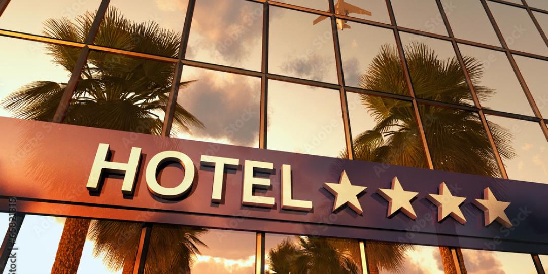 A hotel sign with four stars on a building with the reflection of palm trees and an airplane in the background.