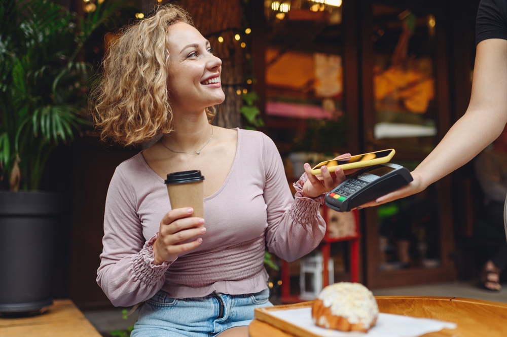 A woman using her phone as a contactless payment option to pay for her coffee and pastry. 