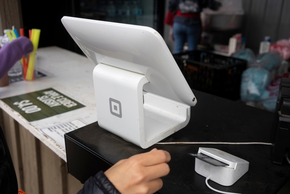 A person paying with a credit card at a square terminal at a shop.