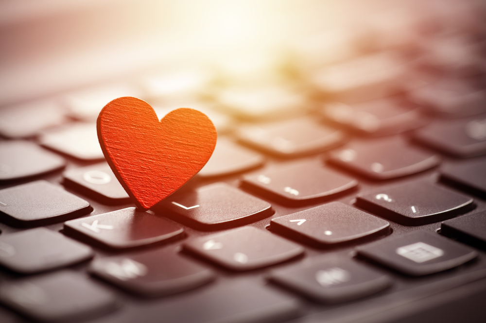 A small red heart resting on a laptop keyboard, which symbolizes online dating.