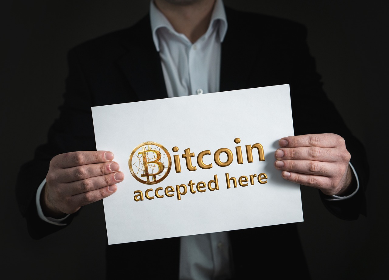 A man holding a sign reading “Bitcoin accepted here”
