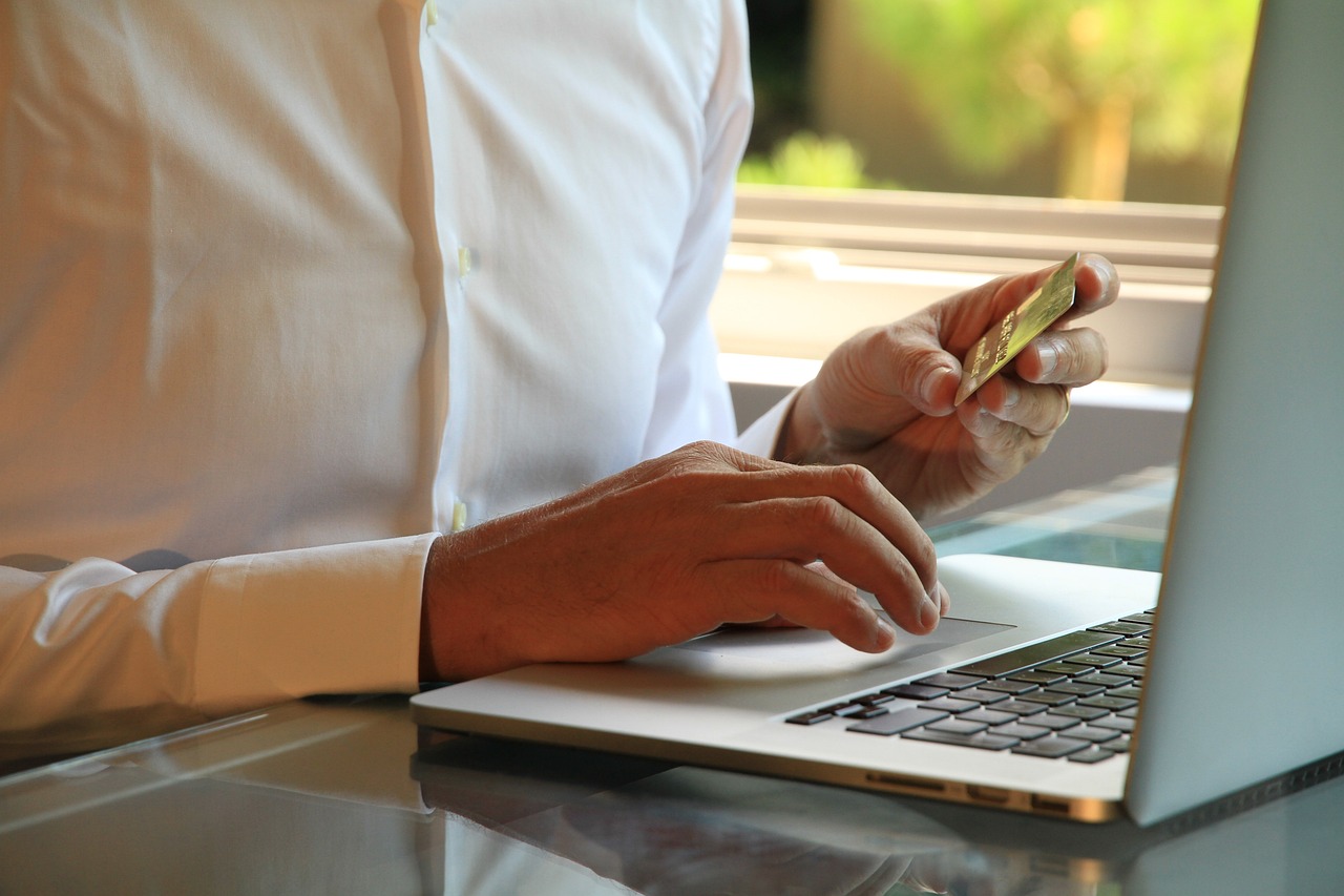 A person with a bank card in their hand using a laptop.