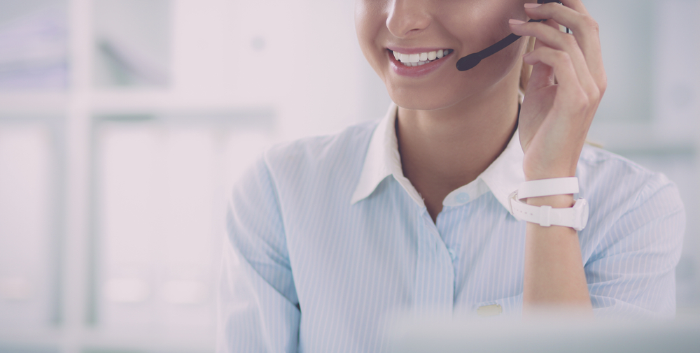 A person smiling and answering a customer service call with a headset.
