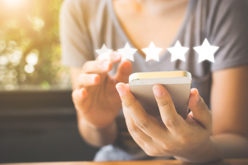A person holding their phone with five white stars above it gives a merchant service  provider a 5-star rating. 
