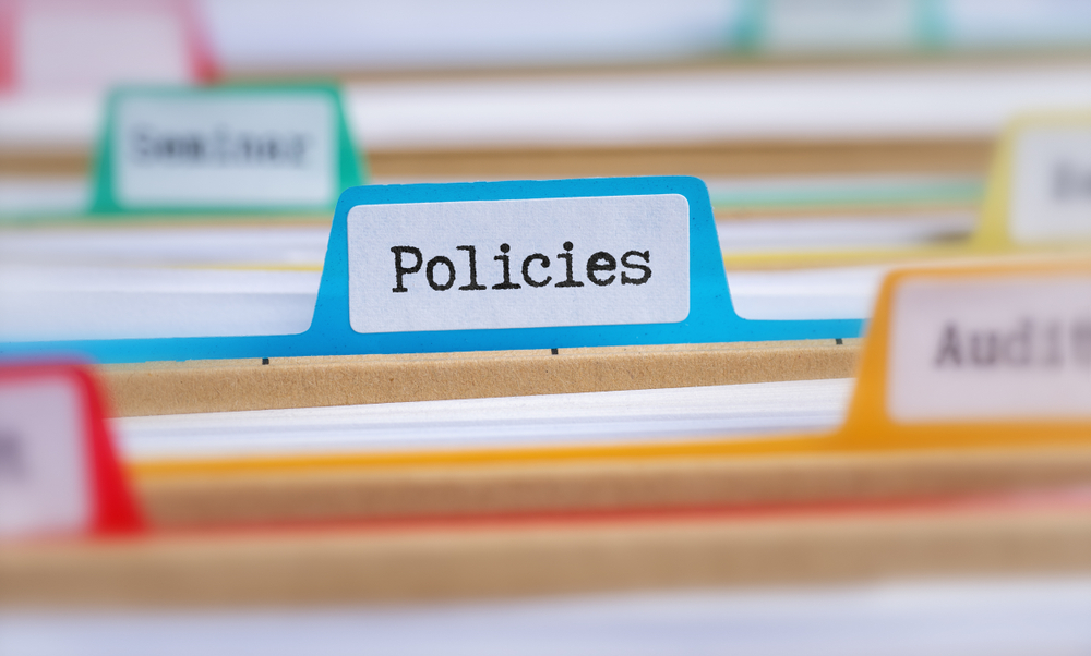 A blue folder in a filing cabinet with other folders that says policies on the tab.