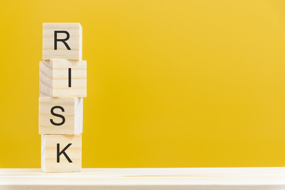 Wooden blocks stacked on top of one another spelling out the word risk with a yellow background.