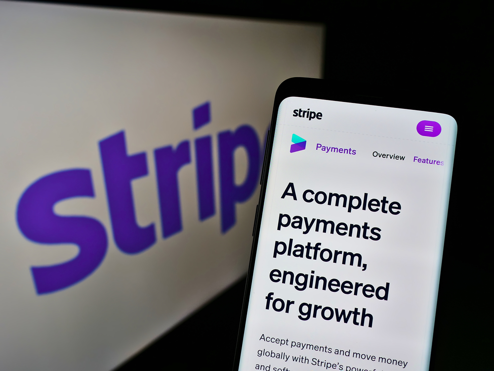 Someone on a mobile phone on the Stripe website with the Stripe logo on a screen in the background. 