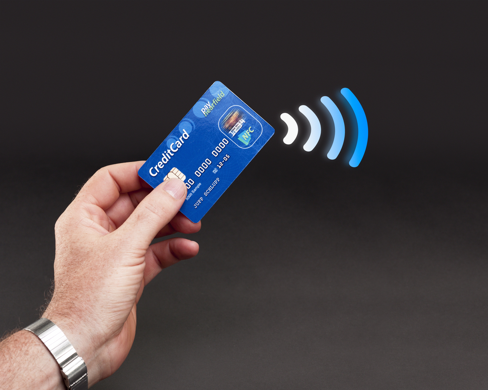 Someone holding a credit card with wireless payment waves coming out of it.