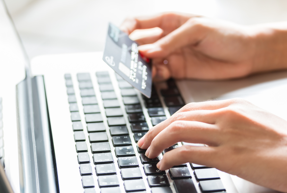 A person using their credit card to make a payment to an e-commerce merchant on a laptop.